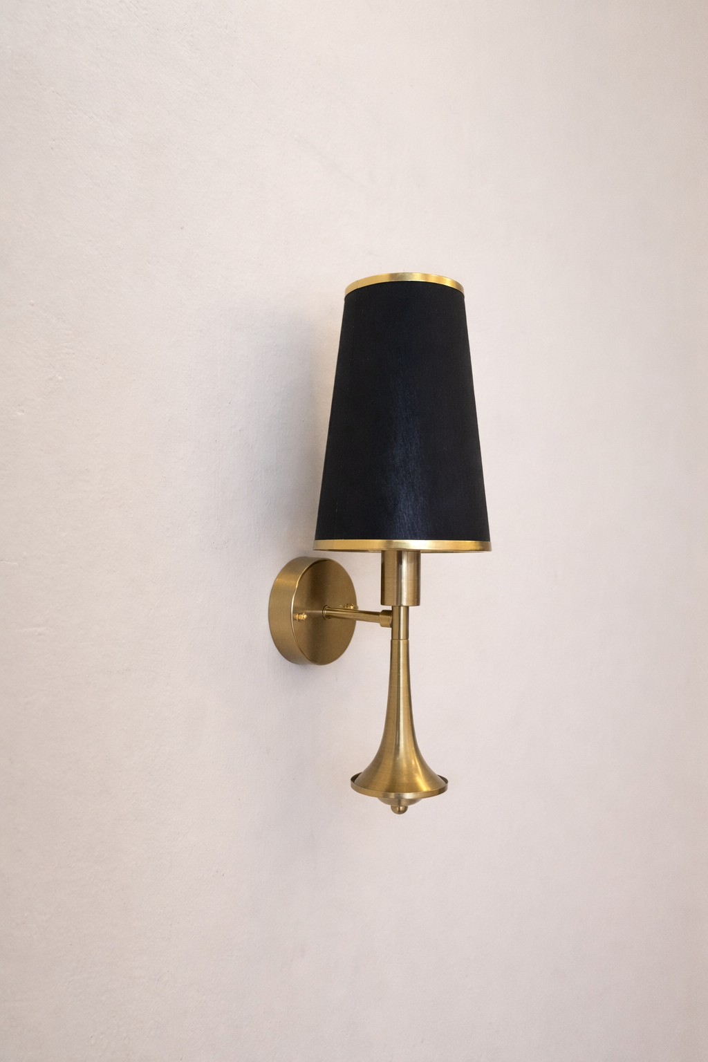 Wall sconce with black shade and brass base on a light beige wall