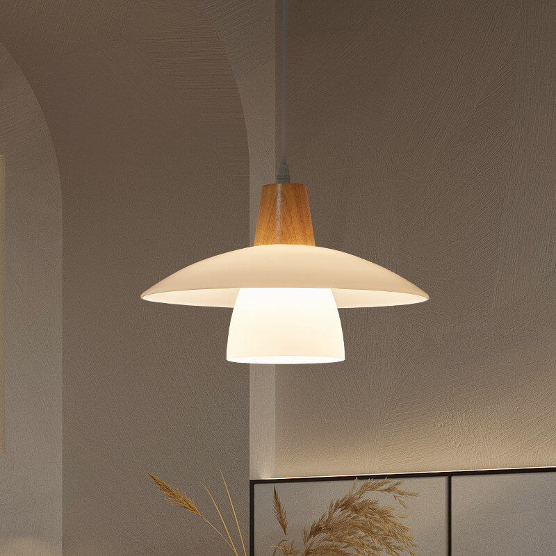 Pendant light with wooden top and white shade hanging against a neutral wall.