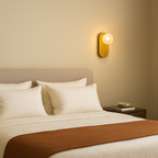 Neatly made bed with white pillows and a brown throw blanket in a softly lit room.