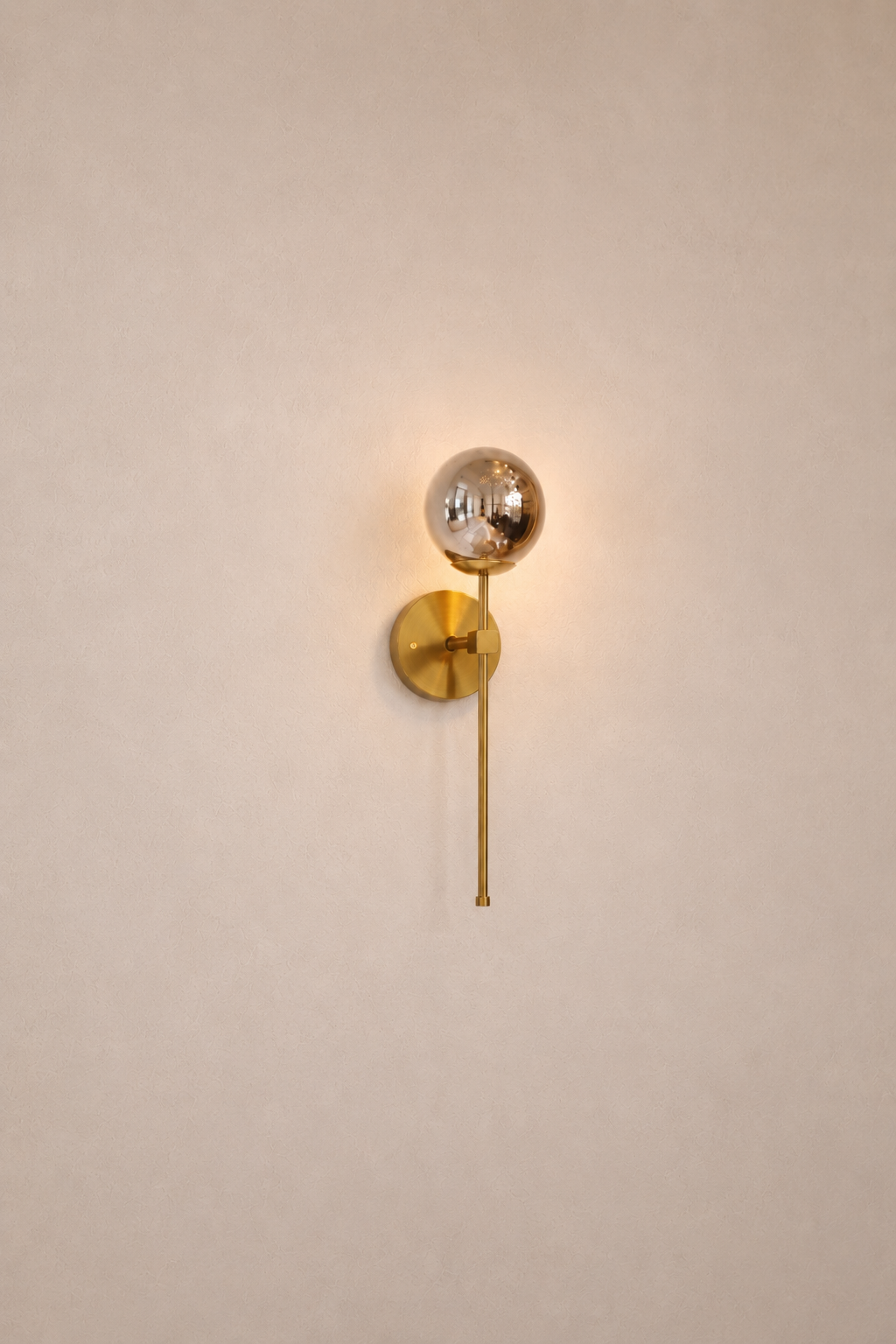Gold wall sconce with a spherical fixture on a beige wall