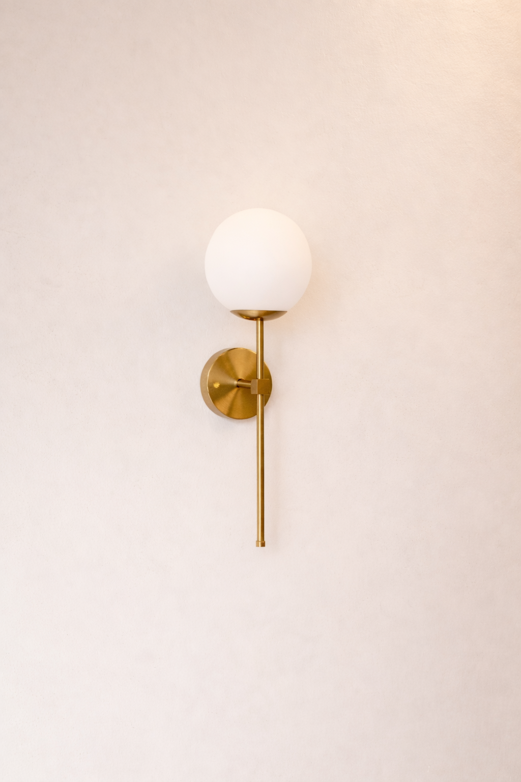 Wall-mounted brass sconce with a white globe on a plain wall.