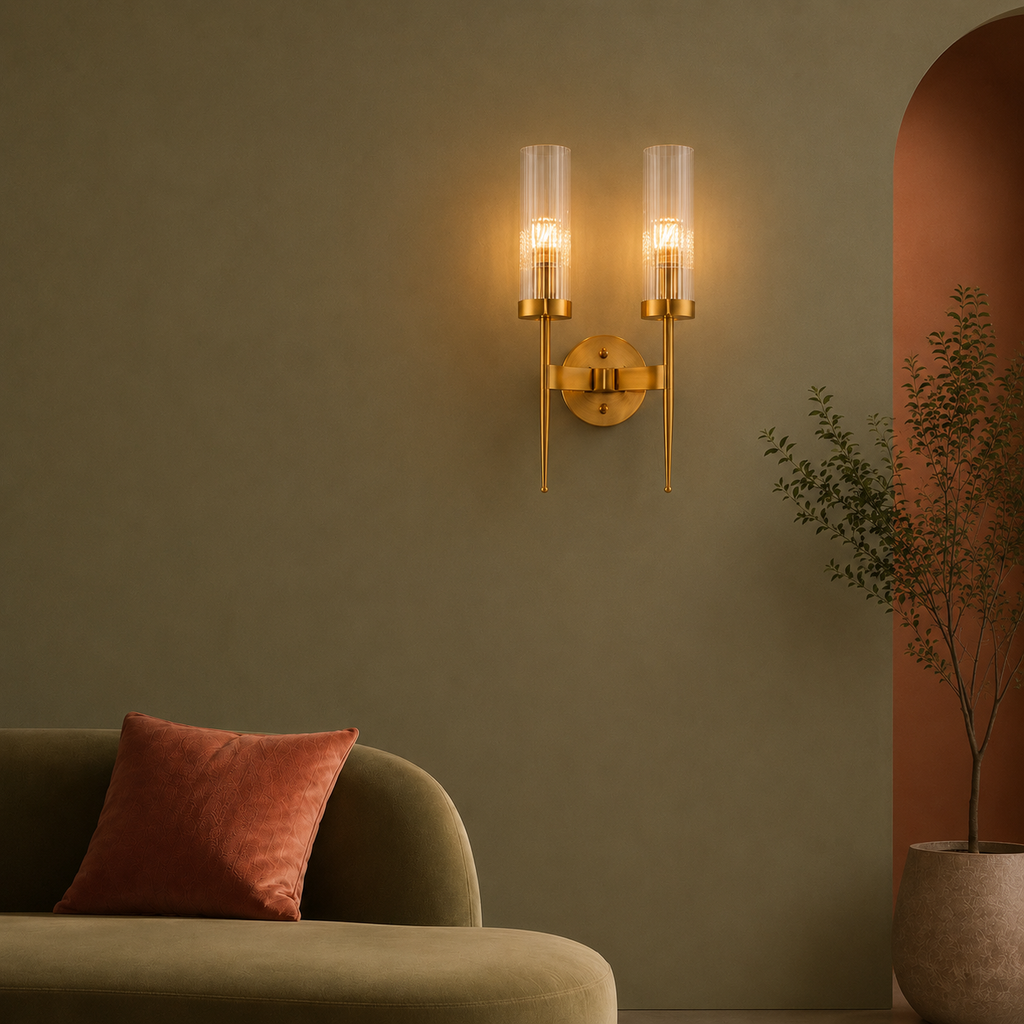 Gold wall sconces on a green wall with a couch and plant in the foreground
