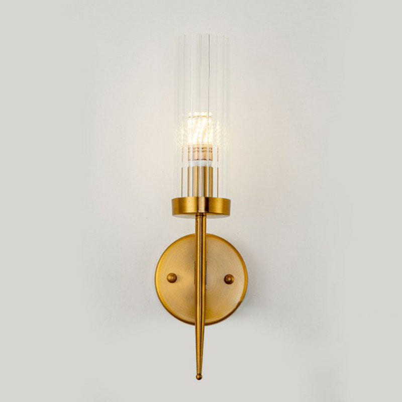 Gold wall sconce with clear glass shade on a light gray background