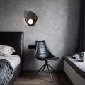 Modern bedroom with a black chair, bed, and wall sconce.