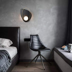 Modern bedroom with a black chair, bed, and wall sconce.
