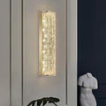 Wall-mounted light fixture on a neutral wall with a dark corner and plant in the foreground.