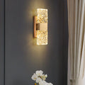 Decorative wall light fixture on a dark wall with a curtain and plant in the background