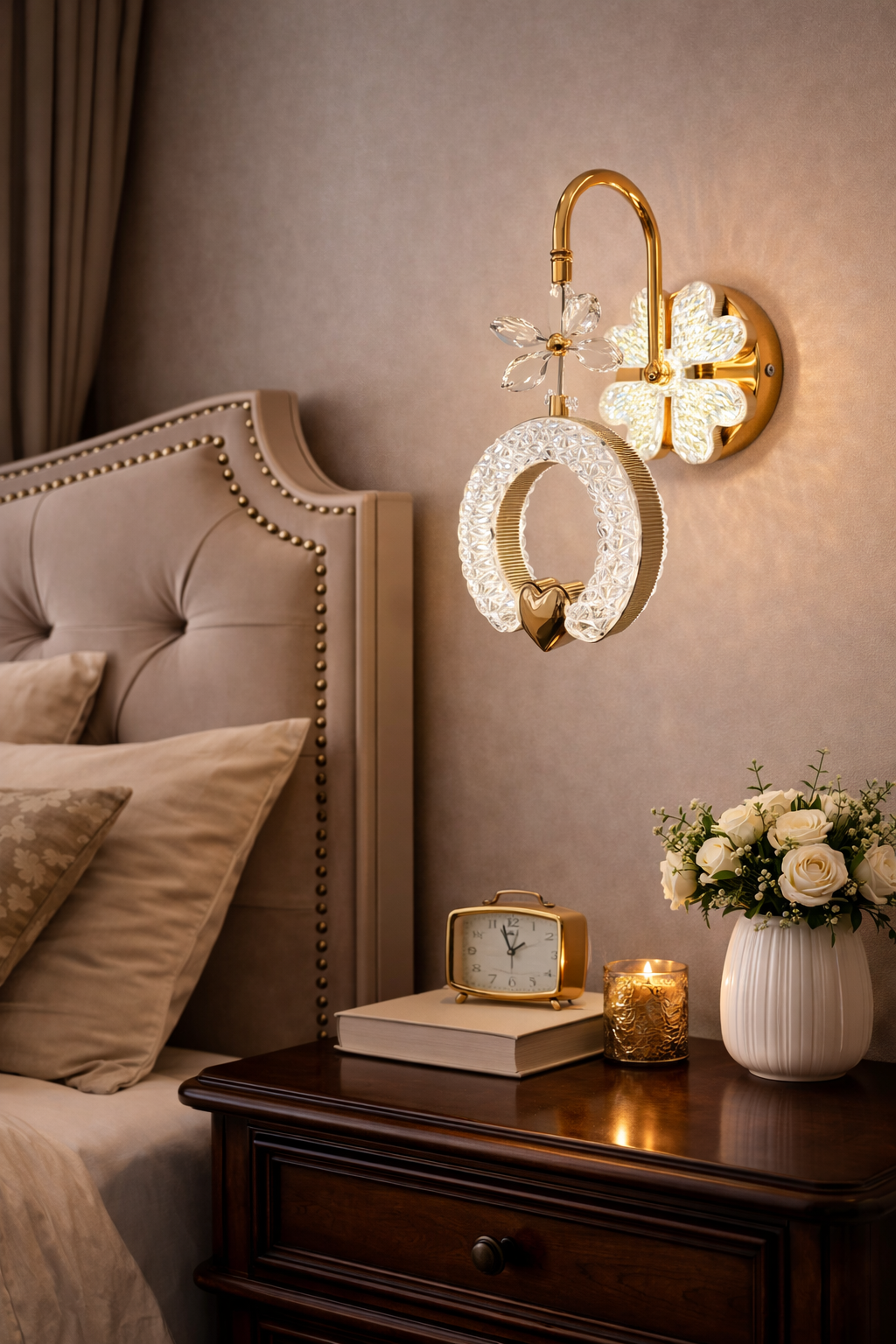 Decorative wall lights above a bed with a nightstand featuring a clock, books, and flowers.