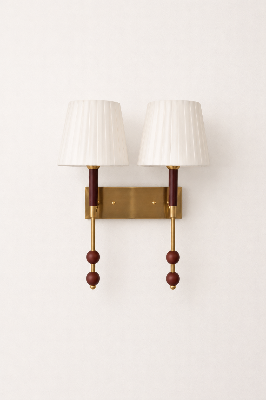 Wall-mounted lamp with two white shades and gold fixtures on a white wall.