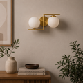 Modern wall sconce with two white glass globes on a neutral wall with decor items below.