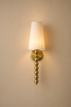 Gold wall sconce with a white lampshade on a beige wall