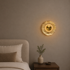 Decorative gold wall light fixture on a beige wall above a bed with a vase and plant on a nightstand.