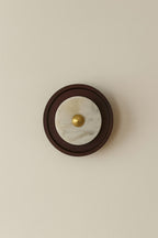 Round wall light fixture with marble center and gold accent on a beige wall.