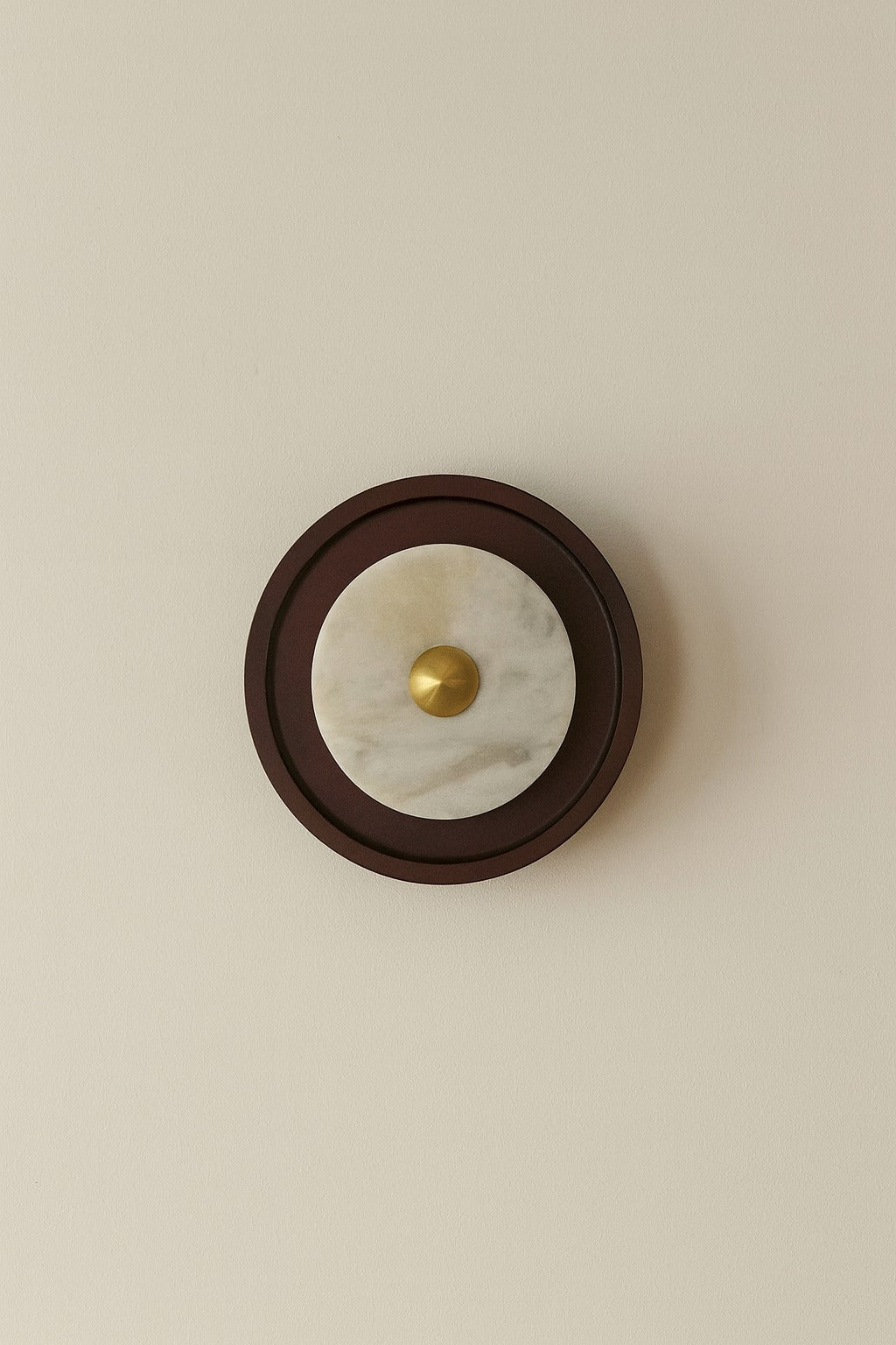Round wall light fixture with marble center and gold accent on a beige wall.