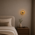 Gold wall sconce on a neutral wall above a bed with a wooden nightstand.