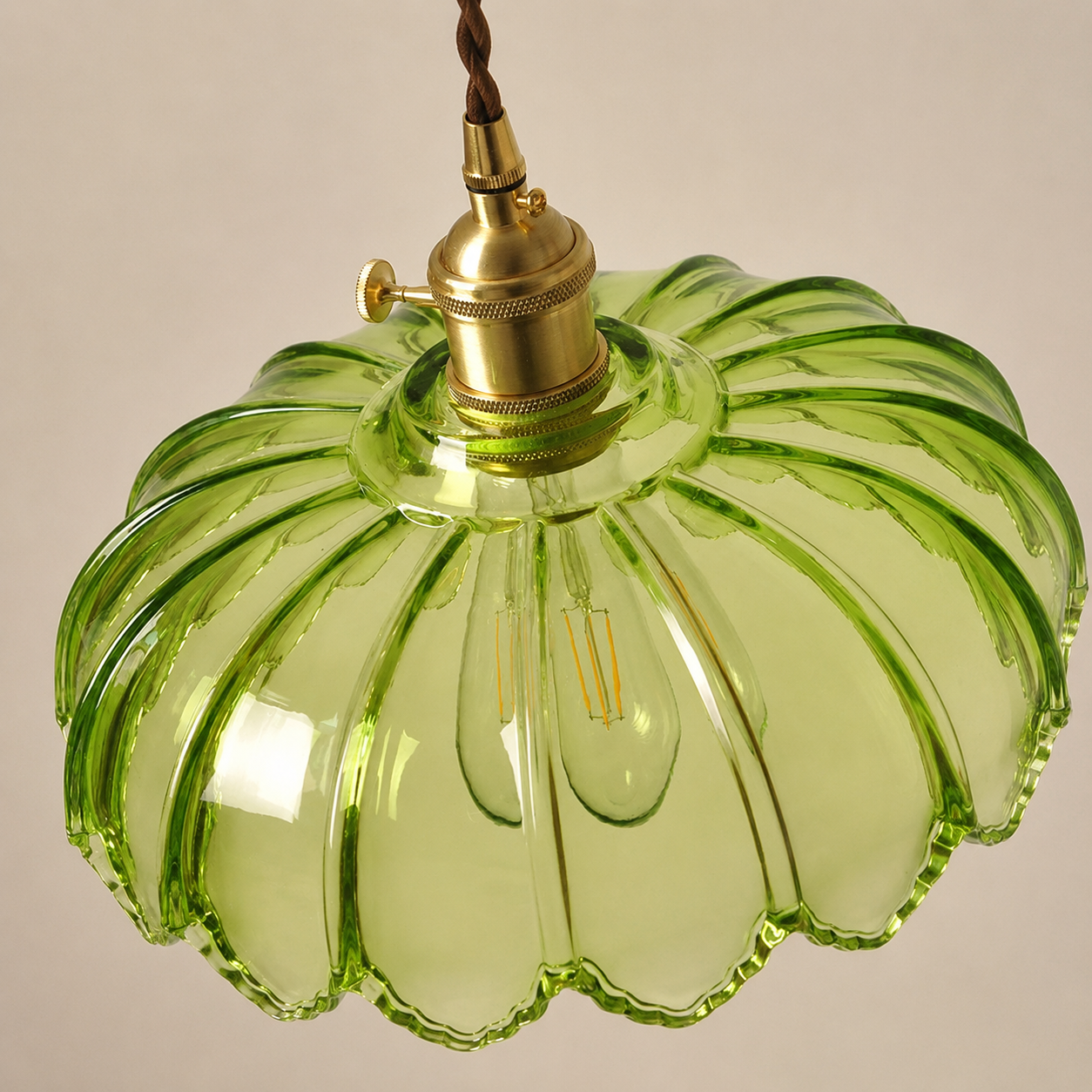 Green glass pendant light with gold fixture on a neutral background
