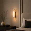 Modern wall sconce in a bedroom setting with a vase and plant on a nightstand.