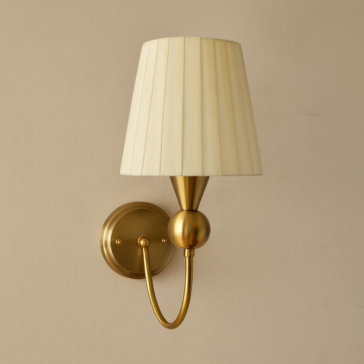 Wall-mounted gold sconce with a white lampshade on a beige wall.