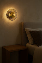 Decorative wall light fixture on a textured wall next to a bed with pillows.