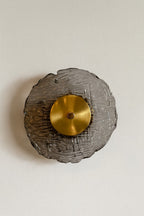 Decorative wall sconce with gold center and textured gray base on a light beige background