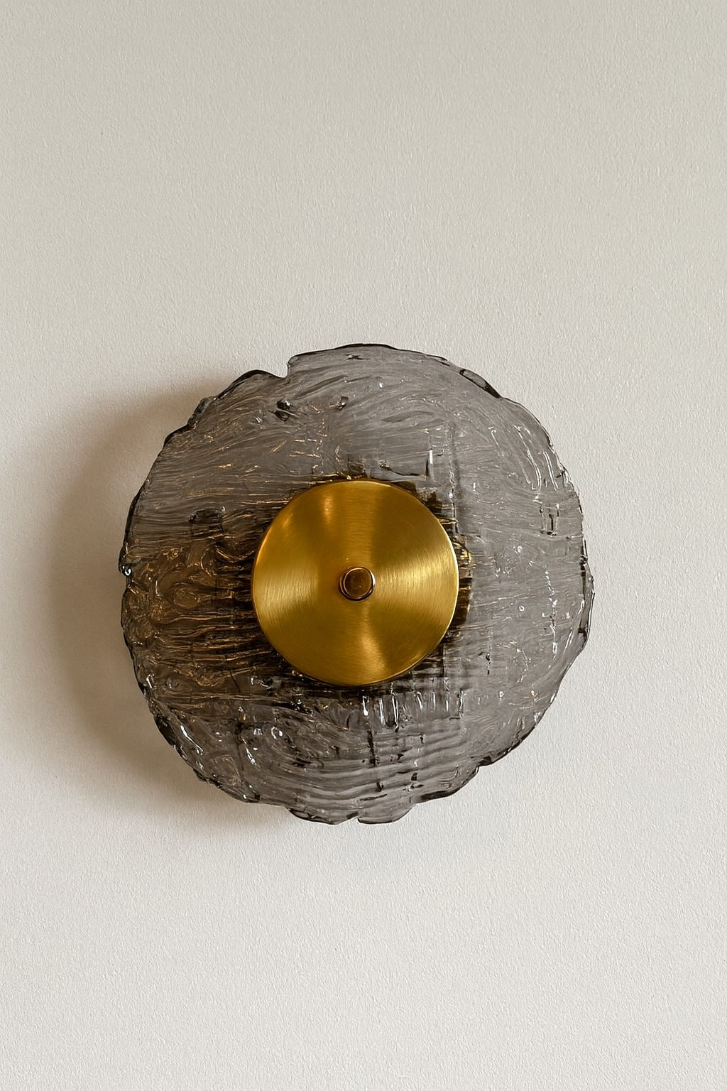 Decorative wall sconce with gold center and textured gray base on a light beige background