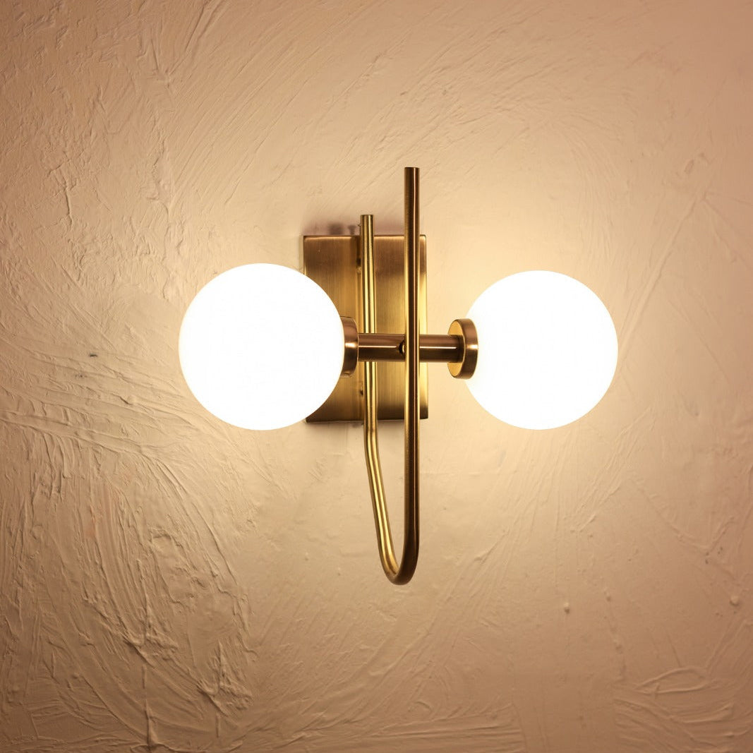 Wall-mounted light fixture with two round glass shades on a beige wall.