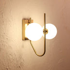 Modern wall sconce with gold fixture and white glass shades on a beige wall.