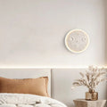 Decorative wall clock on a bedroom wall with a bed and side table in the foreground.